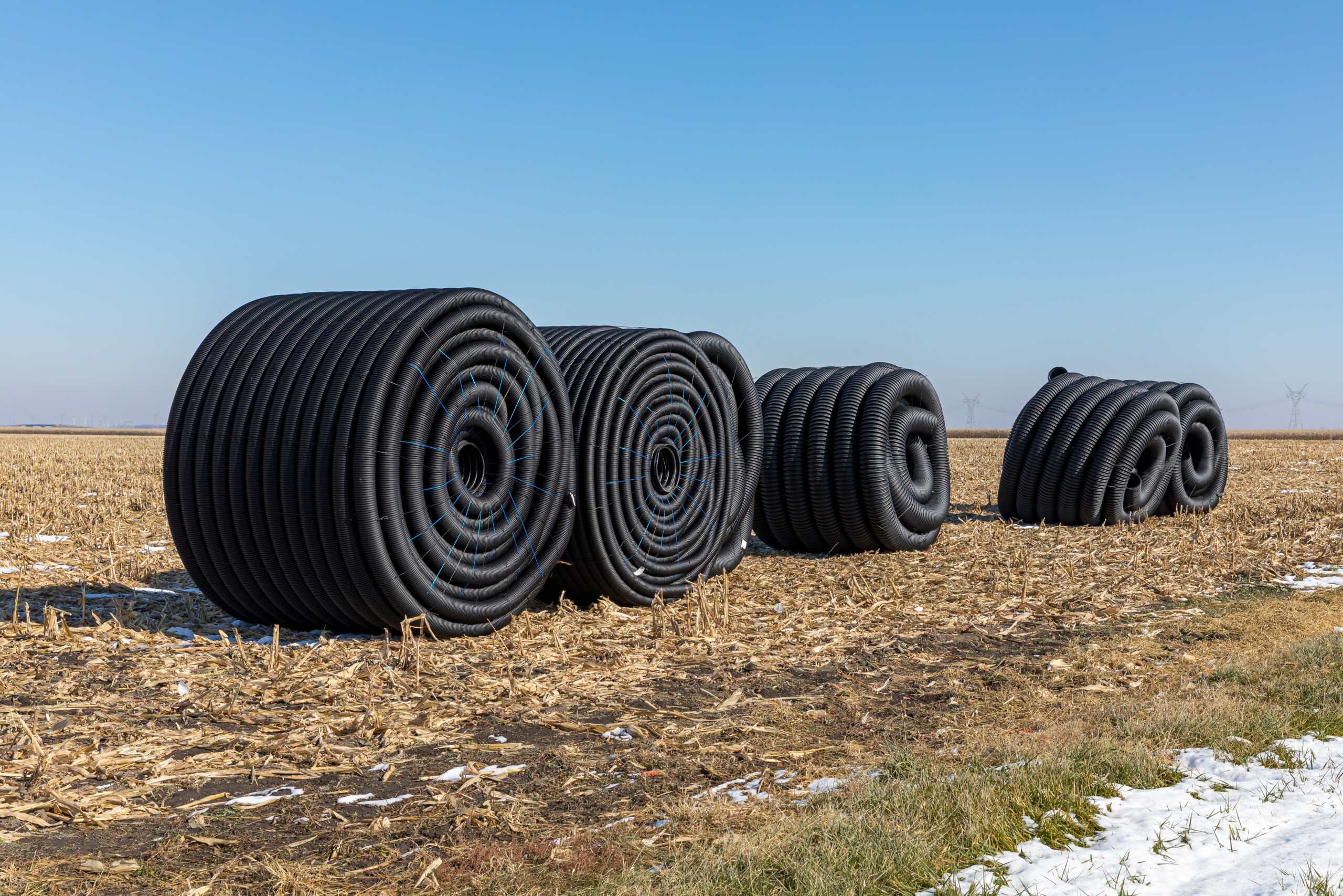 Coiled rolls of black perforated plastic drainage pipe, field tile, sitting in farm field after harvest ready to be buried underground during winter Regional Tile Drainage Program